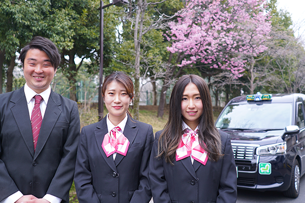 新卒ドライバー3人が桜とJPN TAXIをバックに並んでいる写真